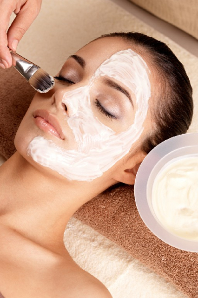 Spa therapy for young woman receiving facial mask at beauty salon - indoors